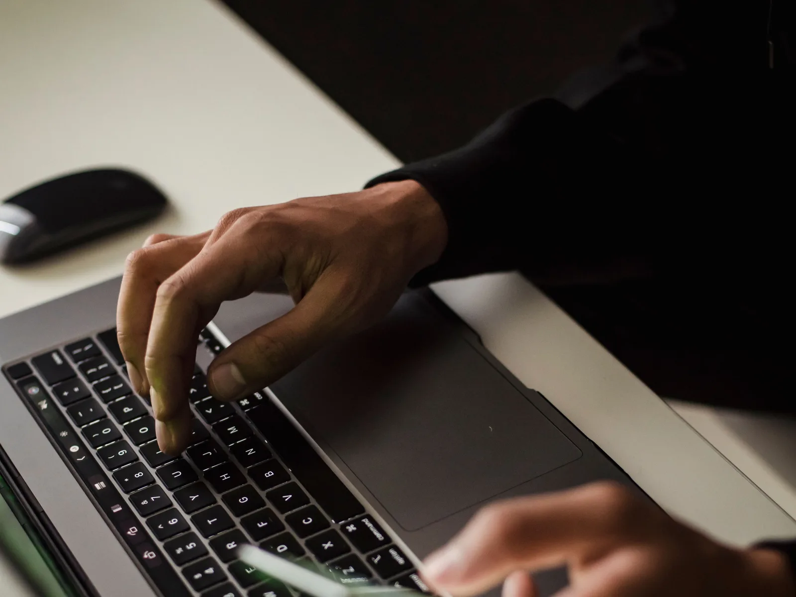 Hands typing on a laptop keyboard while reviewing a project on a phone